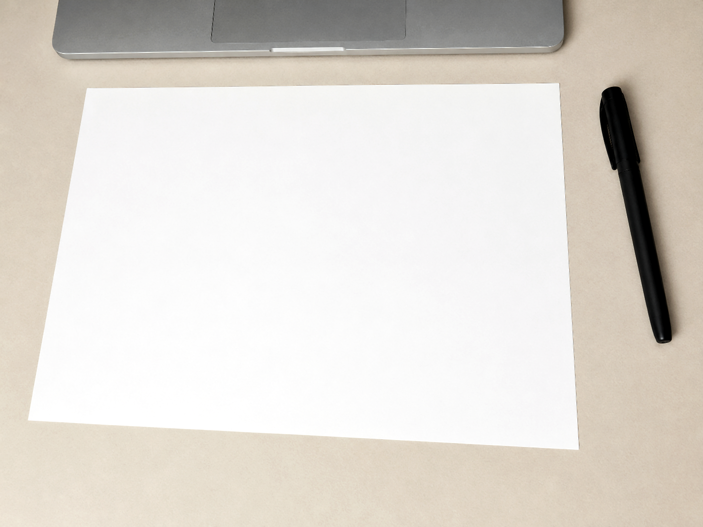 A4 sheet on a beige desk with a MacBook across the top edge and a black pen on the right.
